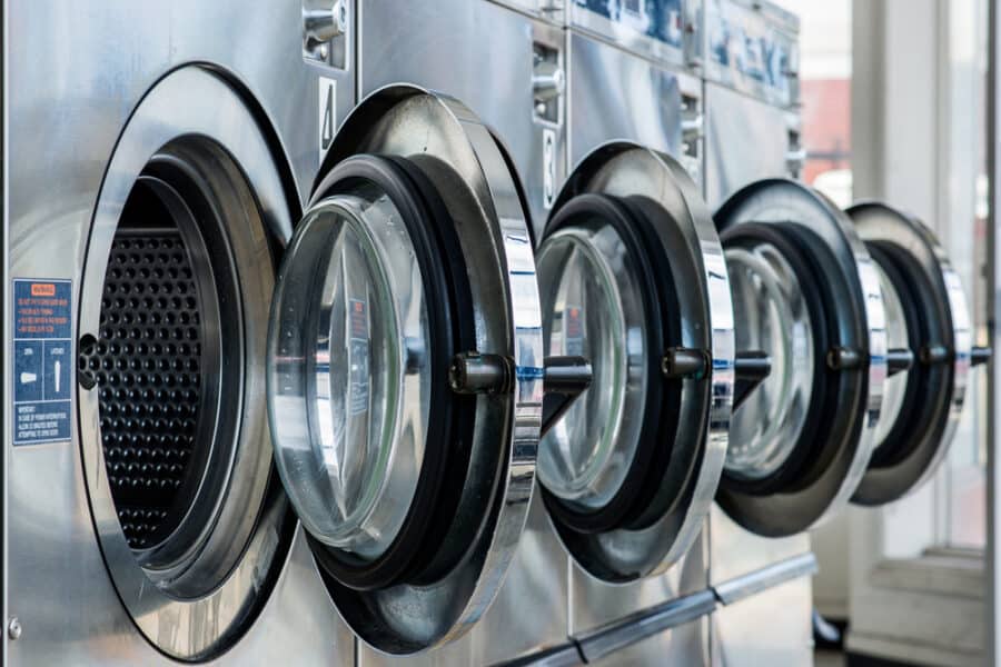 A line of 3 grey commercial laundry machines. Open and ready for clothing.