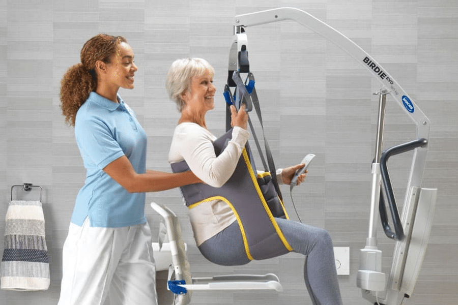 Carer assisting an older woman in a hoist using a patient lifting sling, shown as an example for a how to wash slings guide.
