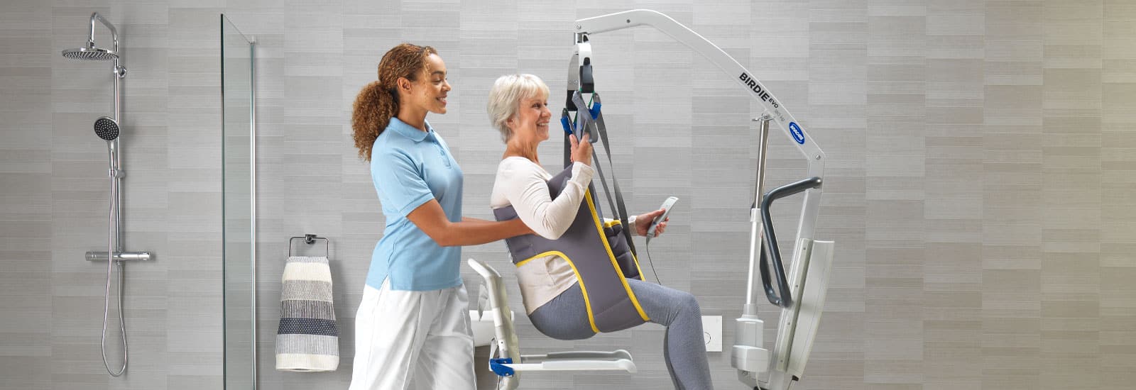 Carer assisting an older woman in a hoist using a patient lifting sling, shown as an example for a how to wash slings guide.